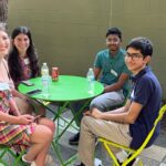 Thumbnail of http://Four%20of%20our%2020%20Under%2020%20gather%20at%20an%20outdoor%20table.