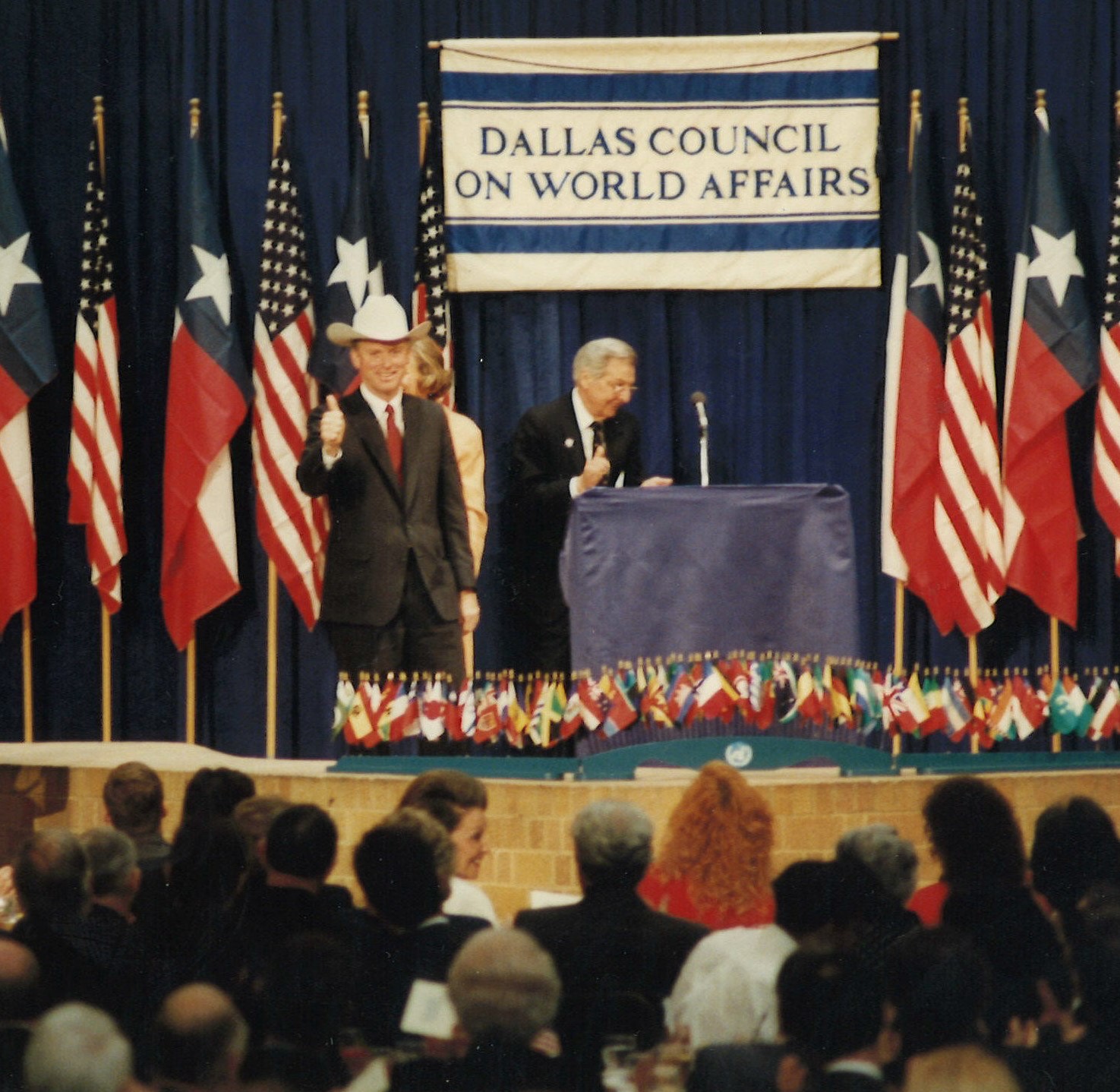 VP Dan Quale wearing a cowboy hat with the flags of the United States of America and the State of Texas behind him